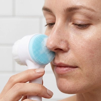 Brosse nettoyante visage bleue appliquée sur la joue d'une femme aux yeux fermés, instant détente
