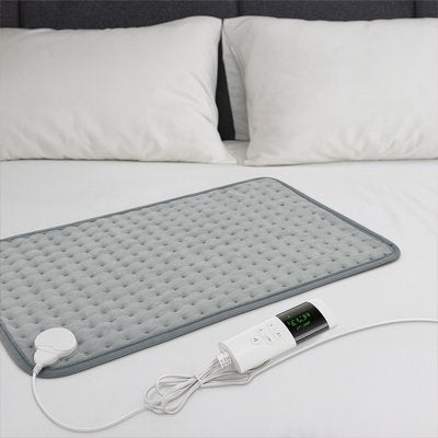 Coussin chauffant gris déplié à plat sur un lit, prêt à l'emploi