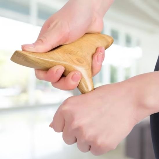 Gua sha en bois passé sur le main d'une personne, soin manuel du corps