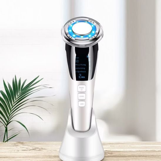 Masseur visage électrique posé sur un meuble, à côté d'une plante verte