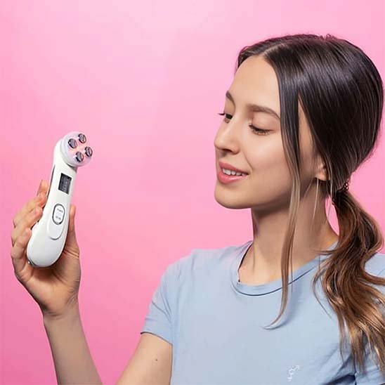 Masseur visage tenu par une jeune femme souriante sur fond rose vif